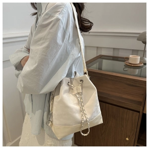 Detailansicht der weißen Kordelzug-Beuteltasche mit Silberkette im Lifestyle-Hintergrund