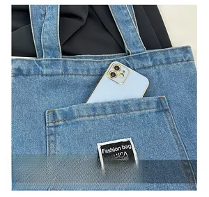 Detailed macro view of the blue denim tote bag featuring an outer pocket with a smart phone