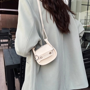 Schicke beige Mini-Satteltasche mit Silberkette, getragen von einem Model im Freien