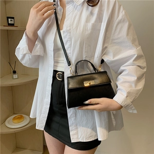 Minimalist black trapezoid handbag with gold metal lock and crossbody strap for women