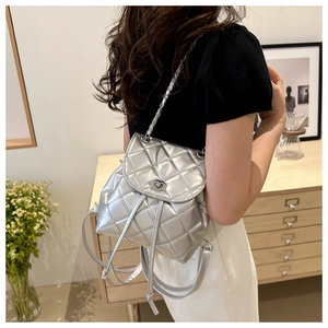 Silver quilted backpack with metallic finish and elegant chain strap shown in modern interior