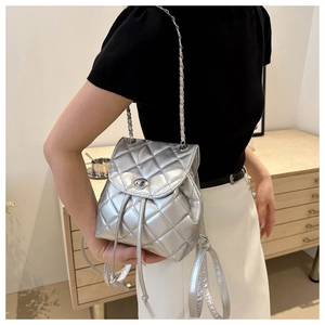 Silver quilted backpack with chain straps shown on a model in a cozy indoor setting