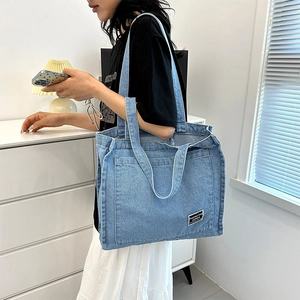 Light blue denim canvas tote bag with wide shoulder strap and minimal fashion label