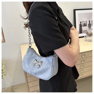 Close-up of a light blue bow shoulder bag with silver chain strap shown in a room