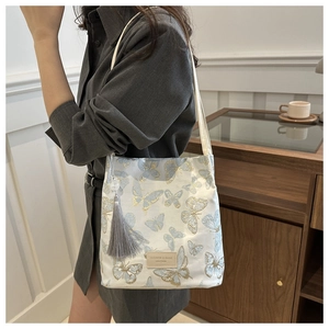 Détail d'un sac blanc avec broderie papillon bleue et charmant pendentif gland