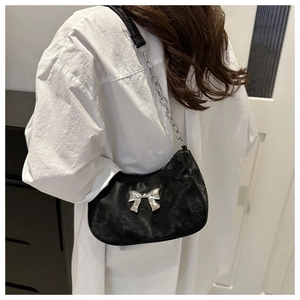 Detail of black hobo bag with metallic silver bow and chain strap on shoulder