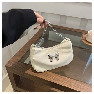 Detail of a creamy white dumpling bag featuring a silver metal bow and chunky chain handle