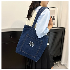 Close-up of dark blue denim tote bag featuring a front pocket with white ACKCA woven label