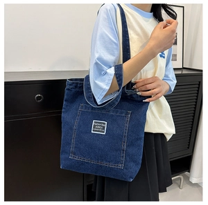 Detail of deep blue denim tote bag featuring a white square fashion label and shoulder straps