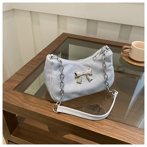 Detailed close-up of light blue shoulder bag with silver bow accent on a coffee table