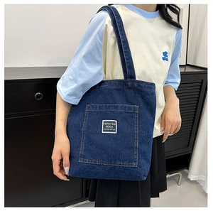 Detail of deep blue denim tote bag featuring large front pocket with white fabric patch