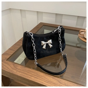 Detail of black fabric underarm bag featuring a large silver metal bow and chunky chain