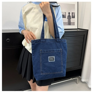 Detailed view of dark blue denim tote bag with large front pocket and white patch