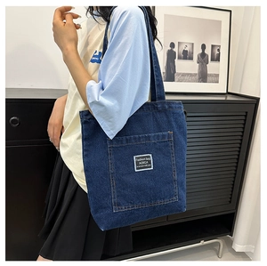 Close-up of deep blue denim tote bag featuring a large front pocket and white woven label