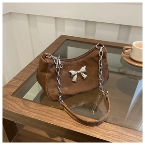 Close-up of brown suede shoulder bag with silver bow detail and chain strap on wood