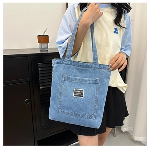 Detail of blue denim tote bag featuring an outer pocket and white brand label on front
