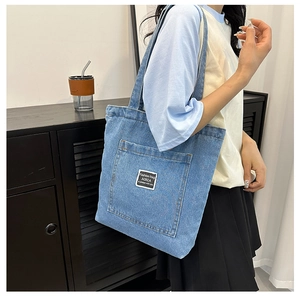 Detail of the blue denim tote bag showing the front pocket and fashion woven label