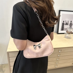 Pink suede underarm bag with silver metal bow and chain strap in a stylish home setting