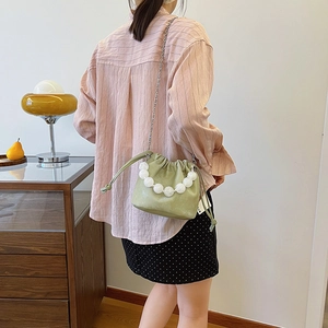 Sac seau vert sauge avec poignée en perles blanches et chaîne argentée porté par modèle