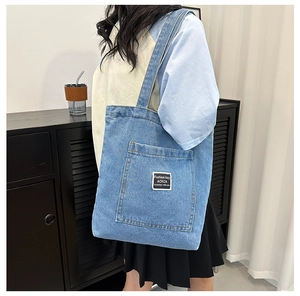 Detail of light blue denim tote bag featuring a large front pocket and a brand woven label