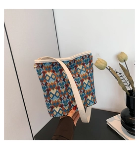 Détail d'un sac seau tissé à motifs géométriques multicolores tenu par une personne en intérieur