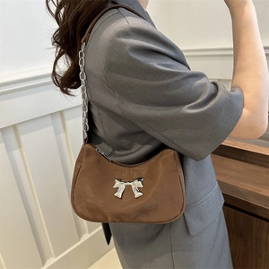 Brown underarm bag with silver metal bow and chain strap worn by model in grey suit
