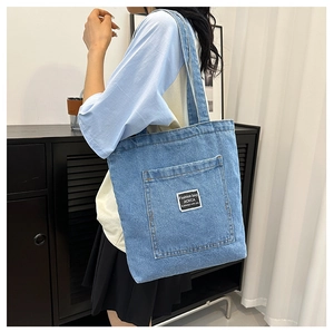 Detail of blue denim tote bag featuring a front pocket with a black fashion logo label