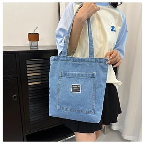 Close-up of washed blue denim tote bag featuring white textile label and stitch details