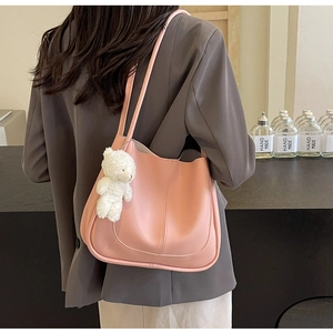 Sac seau en similicuir rose avec breloque d'ours porté par un mannequin en costume gris