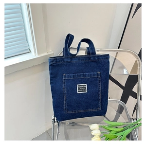 Close-up of deep blue denim tote bag detail showing reinforced stitching and front pocket