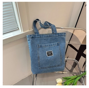 Detail of blue denim tote bag with front pocket and woven label on an acrylic chair