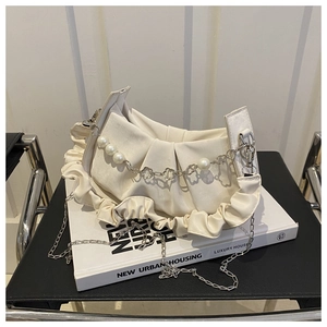 Detalle del bolso nube crema con cadena de perlas y flores metálicas sobre libros