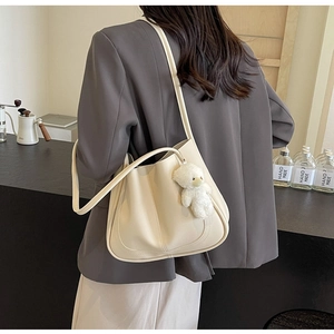 Détail d'un sac seau crème minimaliste avec breloque ours sur un mannequin femme