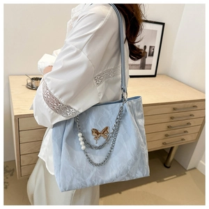 Détail du sac cabas bleu clair avec pendentif papillon et chaîne en perles élégante