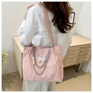 Détail d'un sac cabas rose avec chaînes argentées, pendentif papillon et perles