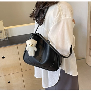 Détail d'un grand sac bandoulière en cuir noir avec un pendentif d'ours blanc mignon