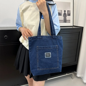 Retro dark blue denim tote bag with front pocket and white label worn by a model