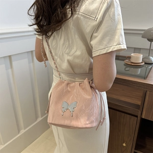 Pink drawstring bucket bag with metallic butterfly and chain strap on a white knit top
