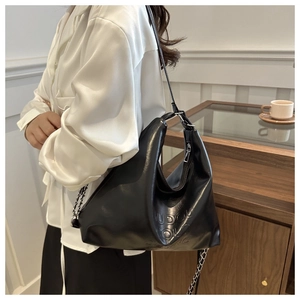 Dettaglio della borsa tote in pelle PU nera con catena metallica indossata da una modella