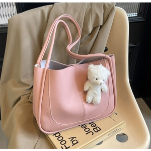 Sac seau en cuir rose mat avec un porte-clés ours blanc sur un fond de siège de couleur beige