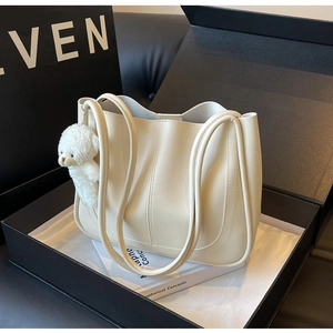 Détail d'un sac cabas en cuir crème avec un charm ours dans un coffret cadeau de luxe élégant