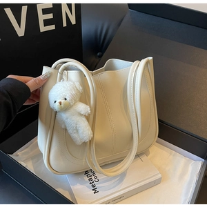 Détail du sac cabas en cuir crème avec coutures verticales et un pendentif ours en peluche
