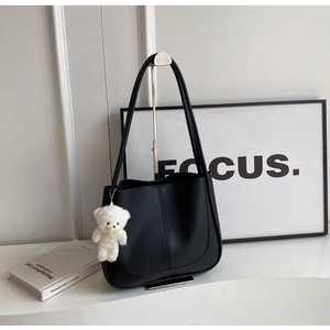 Détail du sac à bandoulière en cuir noir avec breloque ours blanc et surpiqûres verticales