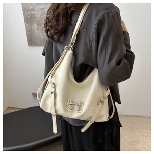 Détail d'un grand sac à bandoulière blanc crème avec nœud argenté et texture en cuir souple