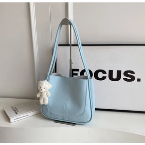 Détail du sac seau bleu clair avec coutures verticales et breloque ours en peluche blanc