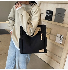 Close-up of black canvas tote bag with side pocket and decorative braided keychain detail