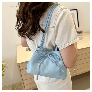 Blue bucket bag with large bow detail worn by model in a cozy indoor setting