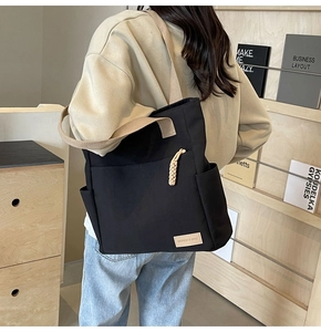 Detail of black canvas tote bag showing wide beige straps and fashion label decoration