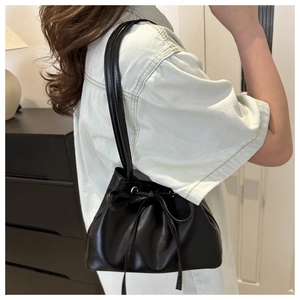 Detail of black drawstring bucket bag showing pleated design and bow closure worn by model