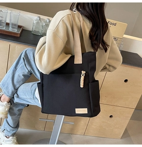 Close-up of black canvas tote bag showing wide beige shoulder strap and fashion label